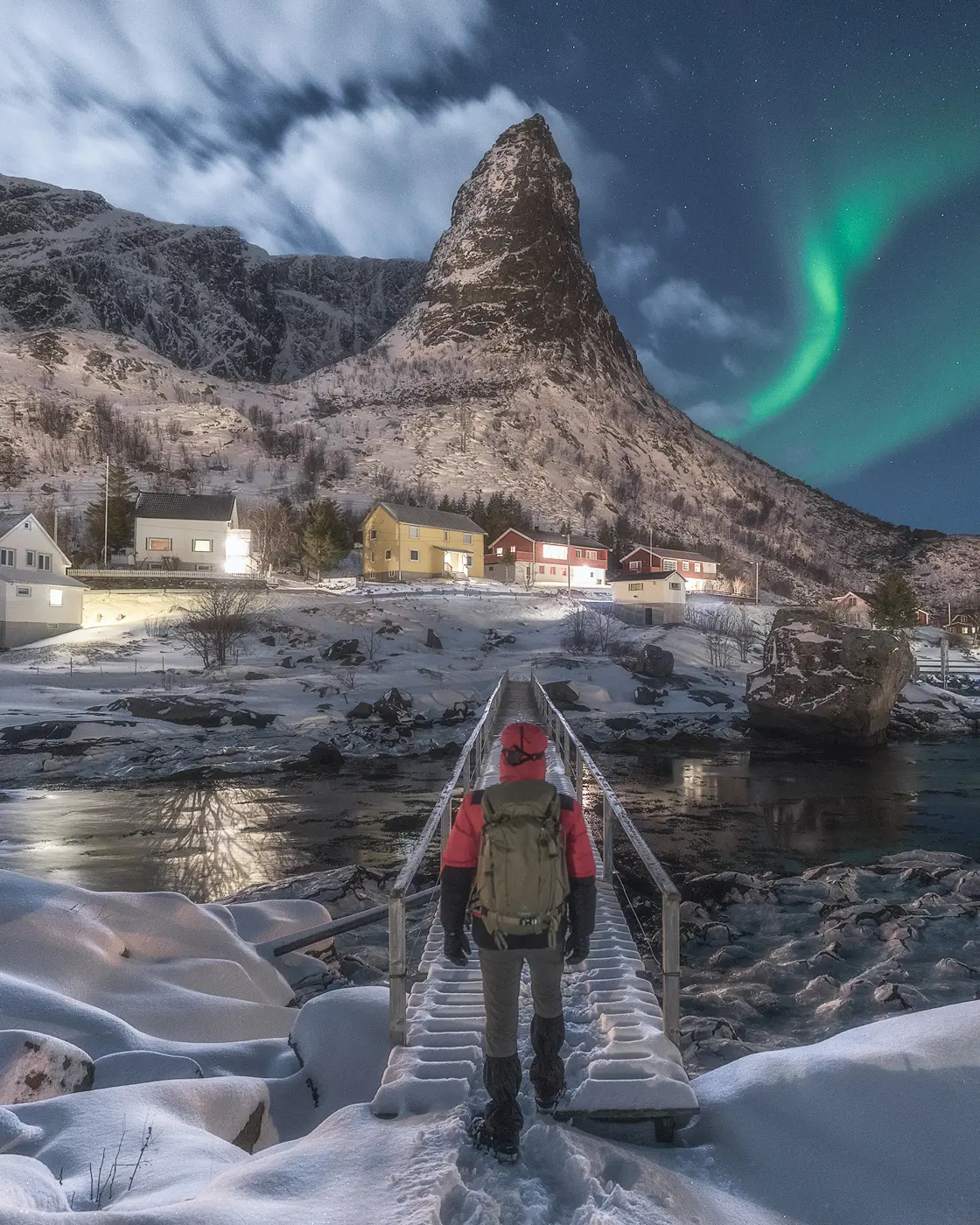 Federico Antonello in Lofoten During Northern Lights Photography Tour Landscape photographer walking in snowy Lofoten village beneath northern lights during winter photography experience