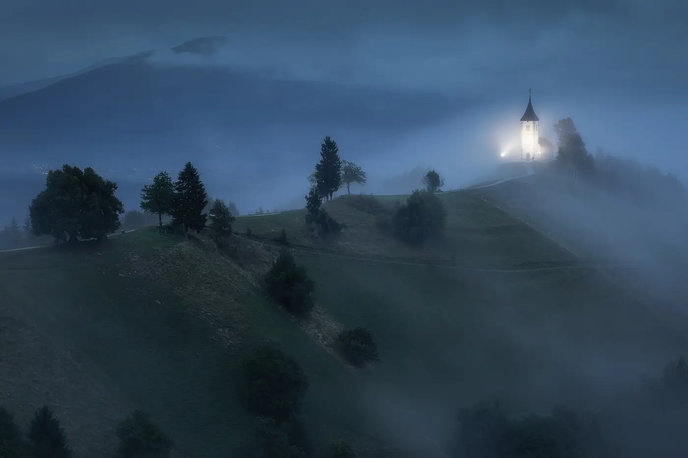 Misty blue hour scene in Slovenia with a church emerging from the fog