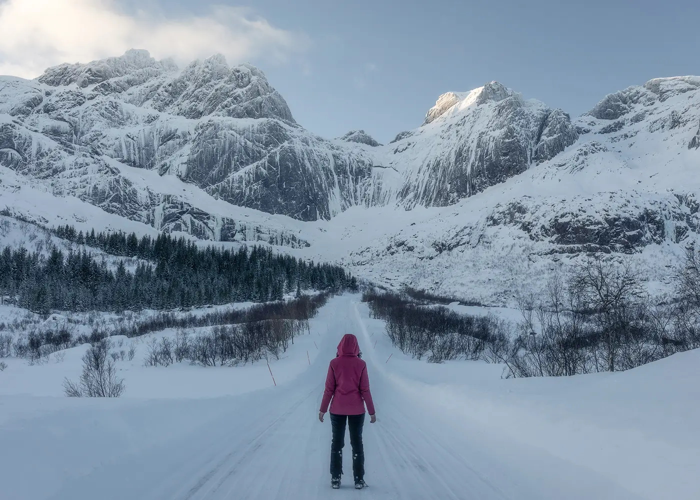 Traveller standing on a snowy road surrounded by dramatic winter mountains in Norway. Atmospheric landscape photography for editorial and tourism use.
