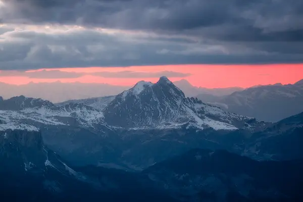 Mountain landscape viewed from Lagazuoi beneath dark storm clouds and a glowing red sunrise in the Dolomites